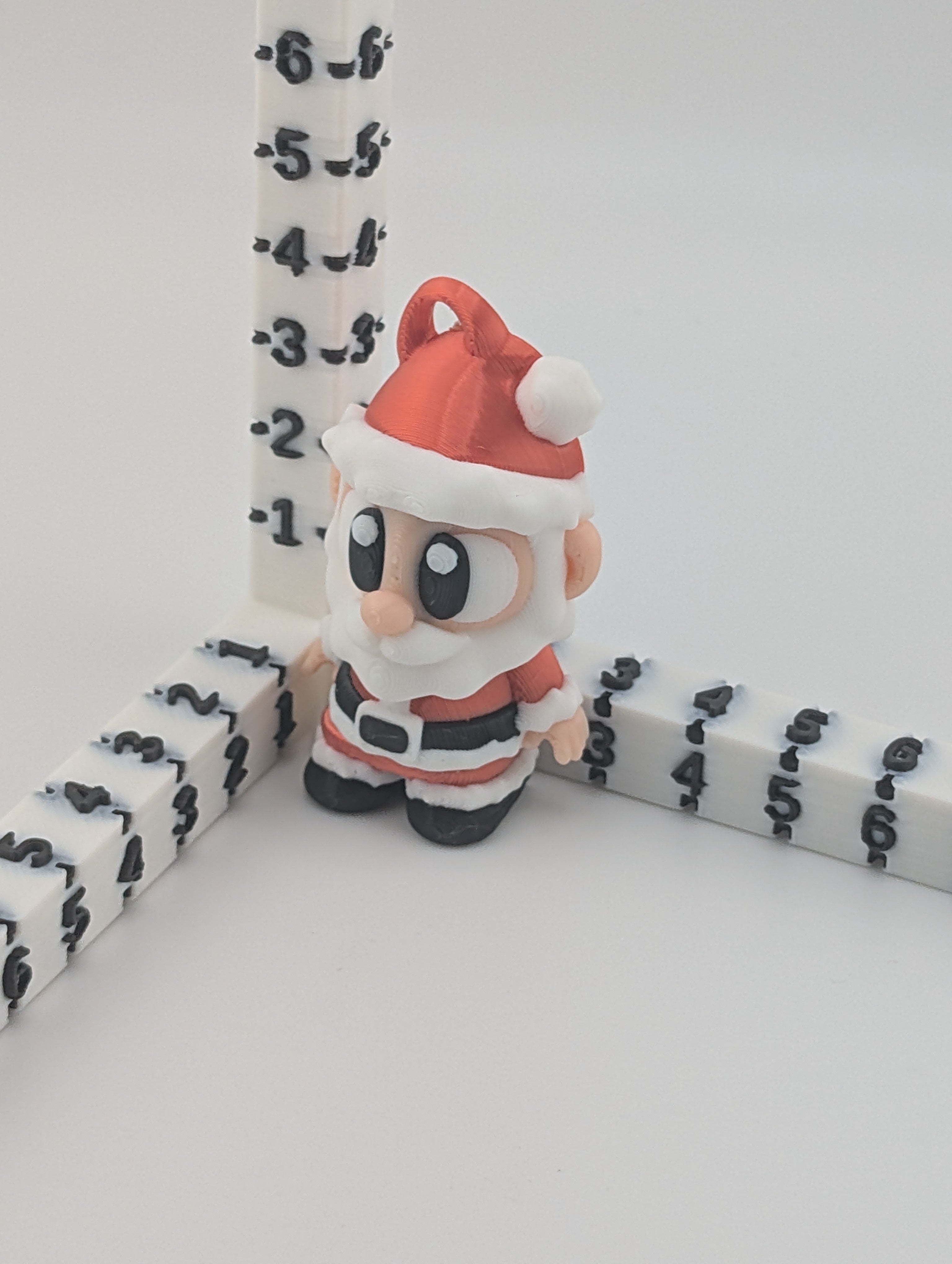 Small figurine of a character in a Santa Claus outfit standing next to a ruler on a white background.