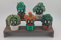 Set of cartoonish cactus figurines on a wooden stand against a plain background